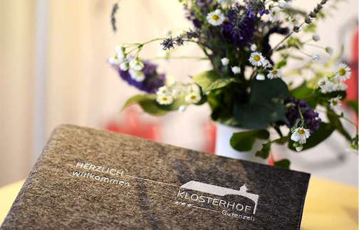 Ein Buch liegt auf einem Tisch, umgeben von Blumen und einer Vase.