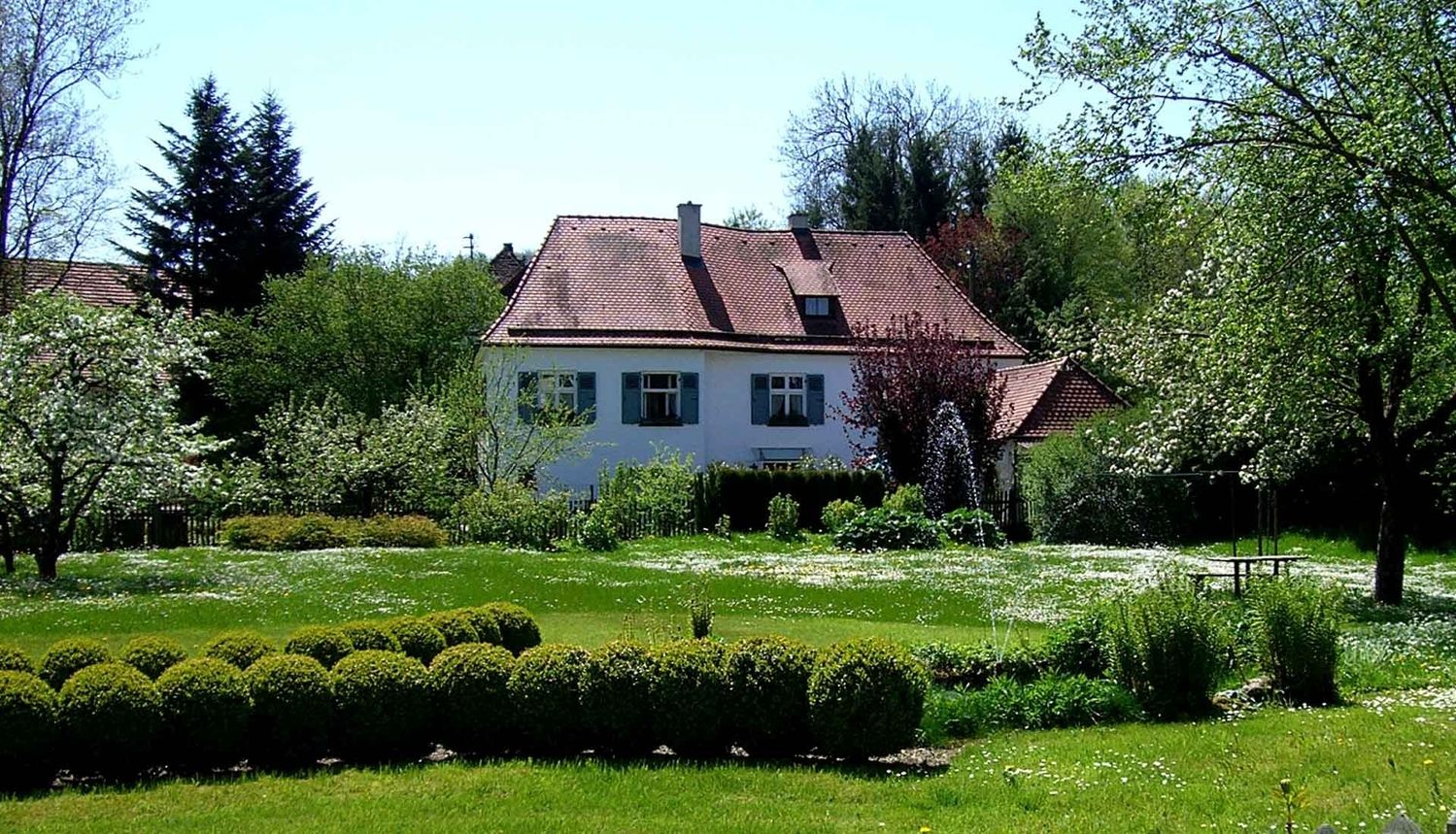 Ein imposantes Haus mit einer grünen Wiese und Bäumen im Hintergrund.